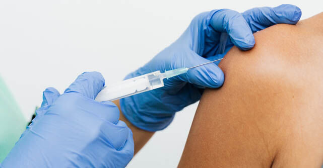 Gloved hands administering an injection into a patient's shoulder