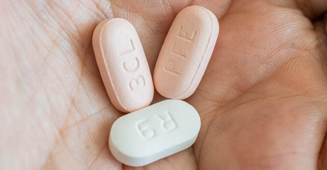 Hand holding three pills imprinted with pharmaceutical codes