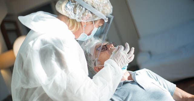Medical worker in protective gear examining an elderly patient's mouth